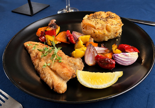 Knusprig gebratenes Fischfilet mit Zitronenscheibe, gegrillten Paprika und roten Zwiebeln sowie goldener Kartoffelgratin mit Kräutern