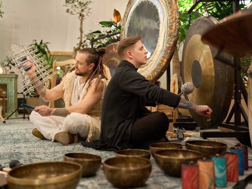 Zwei Klangtherapeuten geben im Spa eine Klangheilungs-Session mit Gongs, Klangschalen und Kristallklängen in einem ruhigen, pflanzenreichen Behandlungsraum