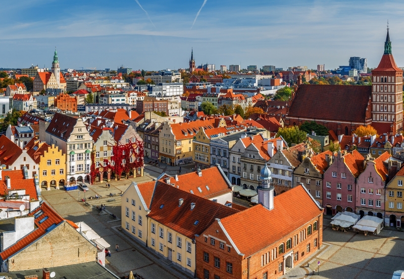 Historischer Marktplatz mit bunten Giebelhäusern, roten Ziegeldächern, Straßencafés und großer Backsteinkirche bei blauem Himmel