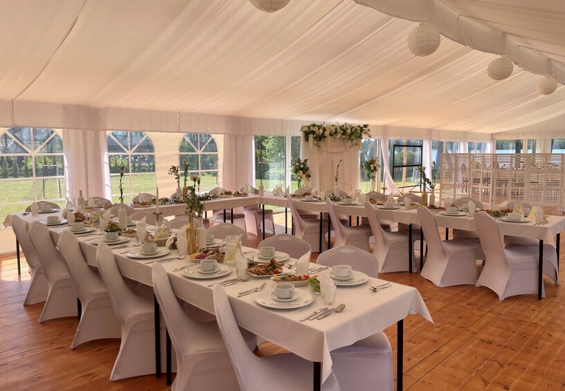 White draped wedding marquee with long linen-covered banquet tables, floral centerpieces, place settings and garden views.