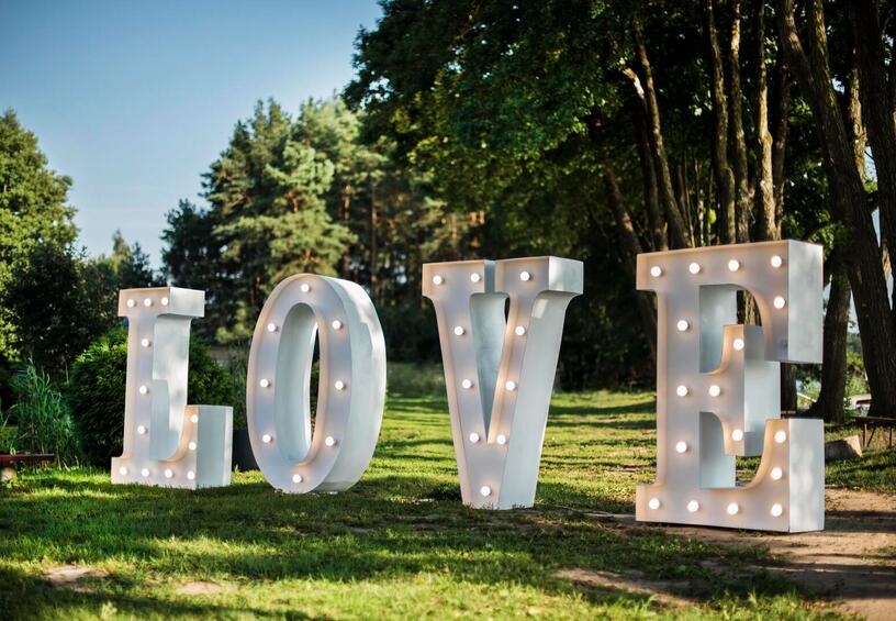 Überdimensionale, beleuchtete LOVE-Buchstaben auf dem Rasen einer Eventfläche, romantische Kulisse für eine Freiluft-Hochzeit.