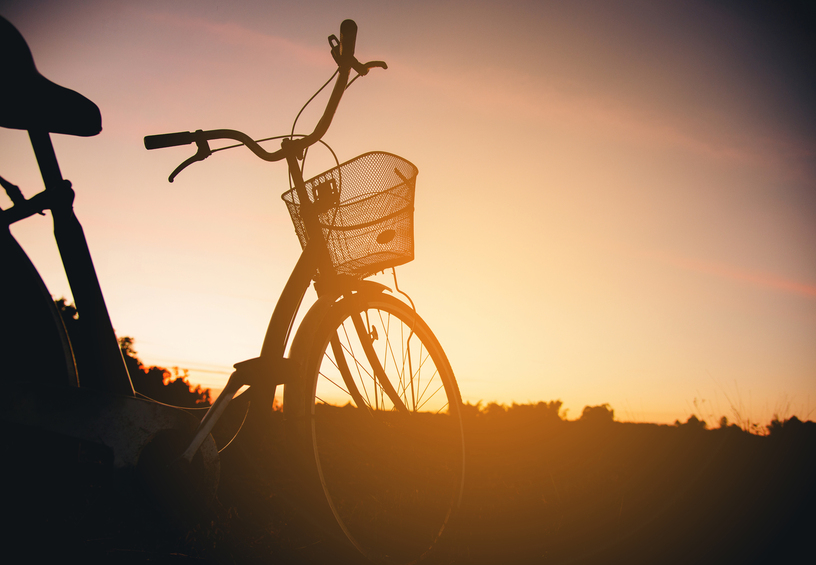 Silhouette of a bicycle with a front basket against a golden sunset over open fields