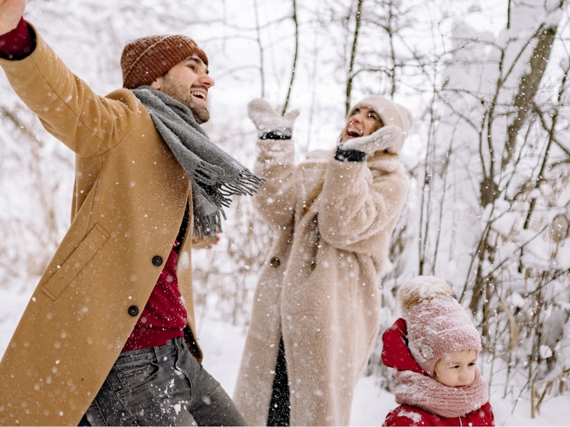 Couple and child bundled in coats and hats laughing and playing in fresh snow in a winter woodland