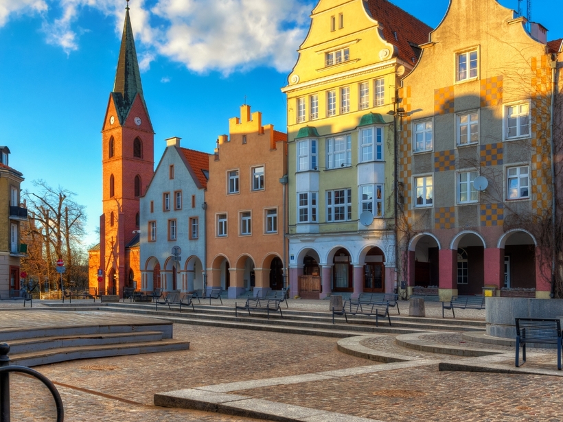 Historischer Marktplatz mit Kopfsteinpflaster, bunten Giebelhäusern, Arkaden und rotem Backstein-Kirchturm