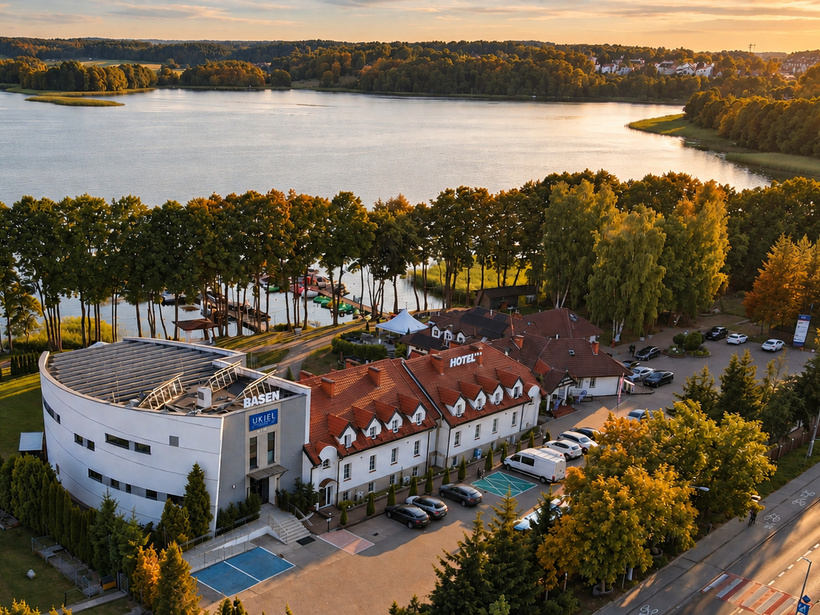 Hotel przy jeziorze z czerwonymi dachami, nowoczesnym budynkiem basenu, pomostem i alejką drzew w złotej godzinie