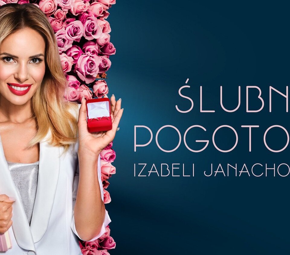 Uśmiechnięta kobieta w białej marynarce przed ścianą róż, trzyma otwarte czerwone pudełko z dwoma obrączkami i notatnik