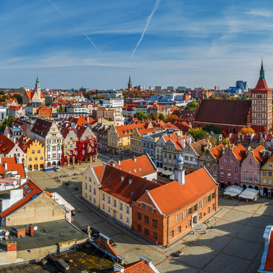 Historischer Marktplatz mit bunten Giebelhäusern, roten Ziegeldächern, Straßencafés und großer Backsteinkirche bei blauem Himmel