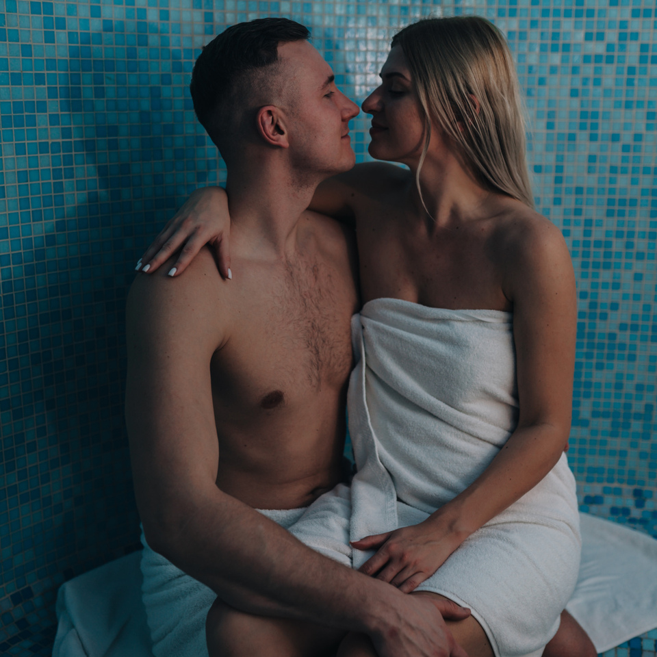 Couple wrapped in towels sharing an intimate moment in a blue mosaic-tiled spa steam room