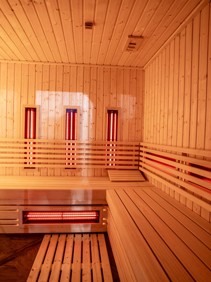 Wood-paneled infrared sauna with tiered benches, headrest pillow and glowing red heaters for a warm, relaxing session