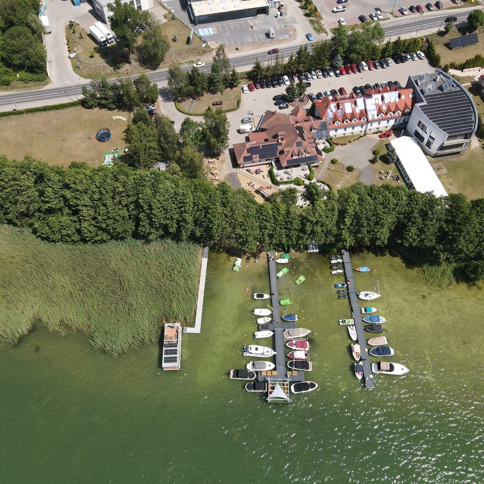 Lakeside hotel complex with red-tiled roofs, marina piers filled with boats and kayaks, docks, tree-lined shore and outdoor terraces