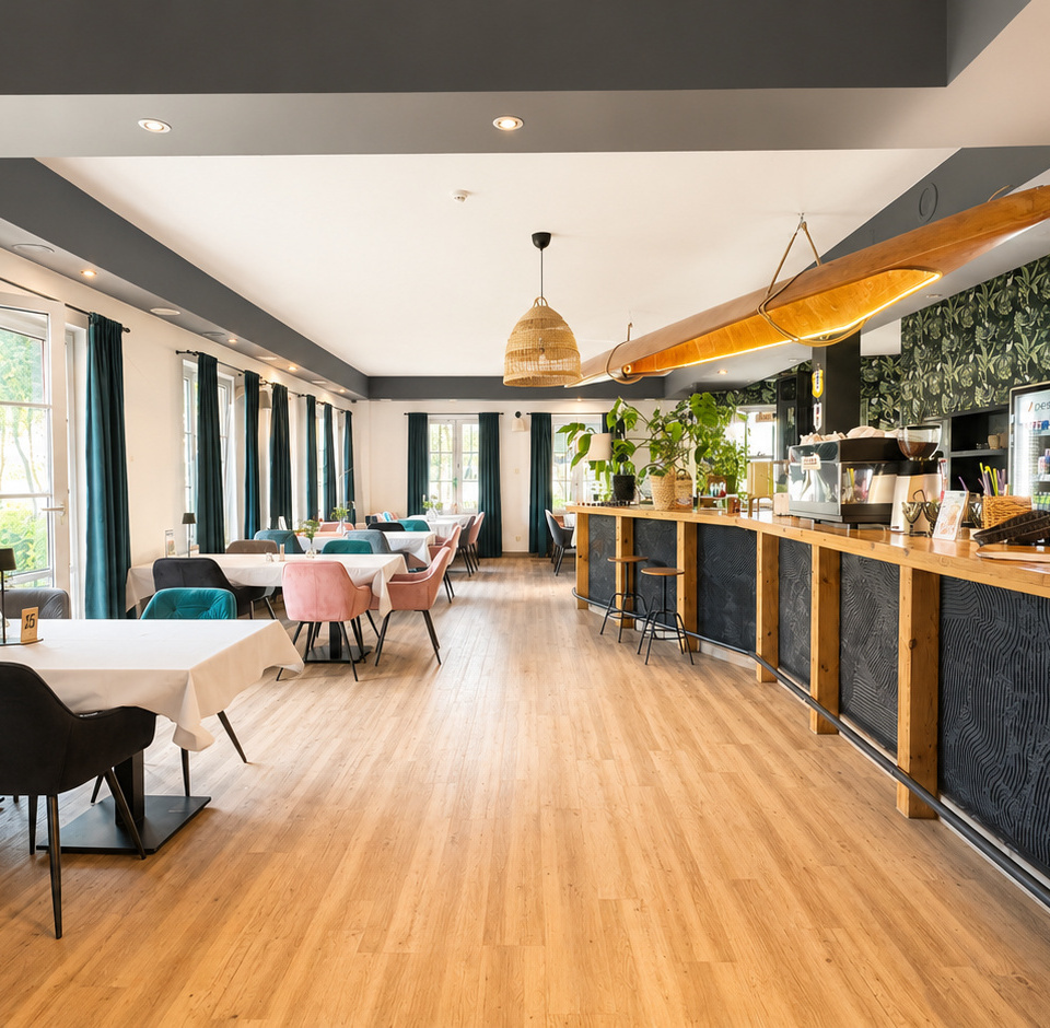 Helles Hotelrestaurant mit Holzbar, Surfbrettlampe, botanischer Tapete, pastellfarbenen Stühlen und Tischen an großen Fenstern.
