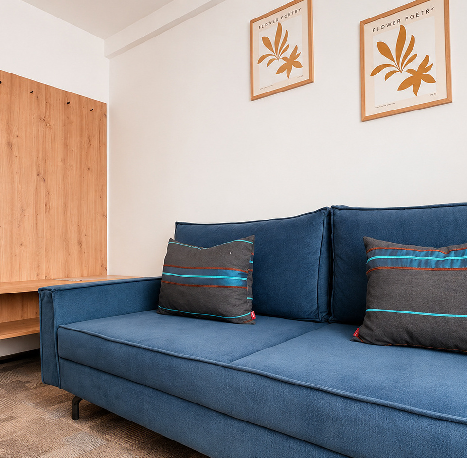 Blaues Sofa mit gestreiften Kissen neben hölzerner Konsole und bodenlangem Spiegel, minimalistische Einrichtung und gerahmte botanische Motive.