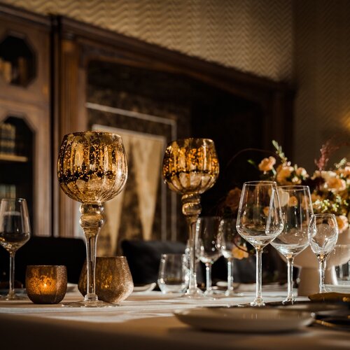 양초 불빛 아래 호텔의 고급 식탁, 금빛 고블렛과 크리스털 와인잔, 꽃 장식과 따뜻한 원목 선반이 배경에.