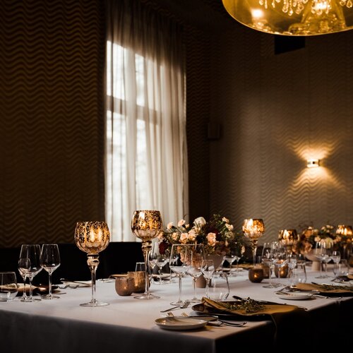 화이트 리넨 깔린 세련된 프라이빗 연회 테이블, 꽃 장식과 금빛 캔들 홀더, 와인잔들