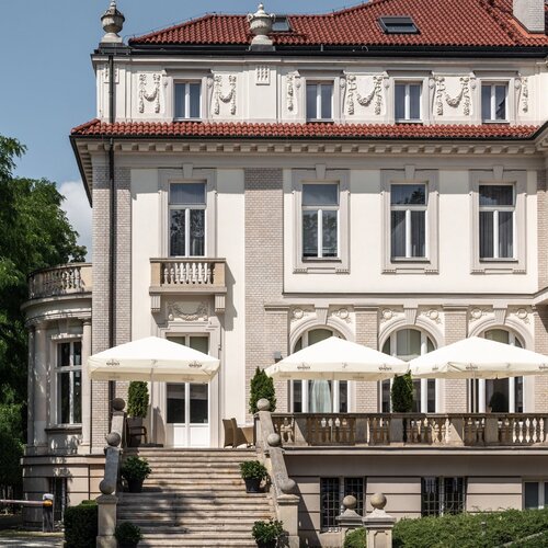 우아한 역사적 빌라형 호텔, 석조 계단이 크림색 파라솔과 야외 좌석이 있는 테라스로 연결됨