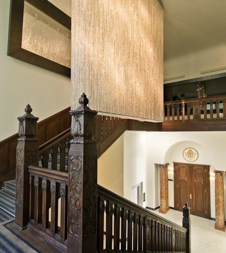 Wytworne lobby z rzeźbionymi drewnianymi schodami i balkonem, kaskadowa kryształowa kurtyna-żyrandol i marmurowe wejście.