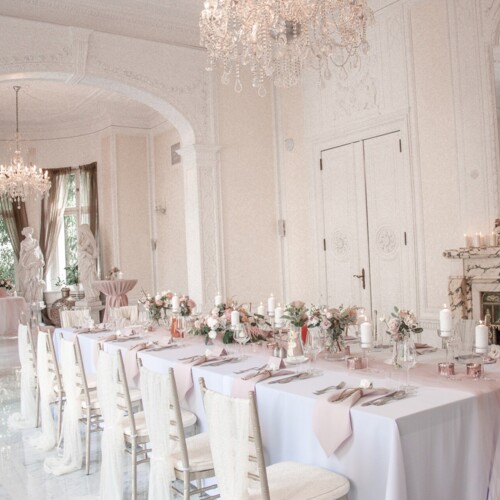 화려한 연회장, 긴 웨딩 테이블과 분홍 테이블 러너, 꽃장식, 촛불, 크리스털 샹들리에와 대리석 벽난로