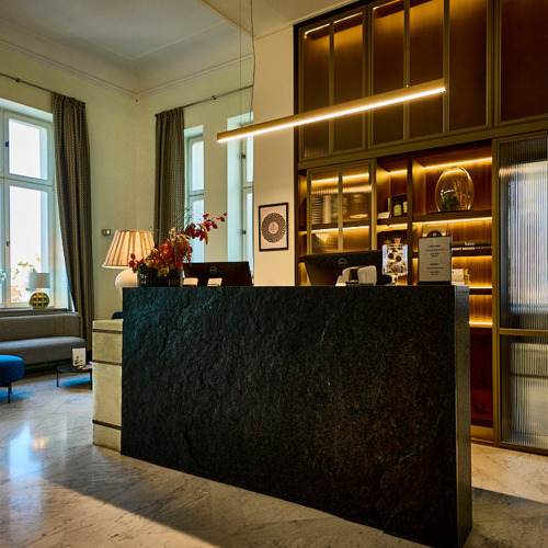 Recepcja hotelowa z ciemnym kamiennym barem, podświetlanymi drewnianymi półkami, marmurową podłogą i strefą wypoczynkową