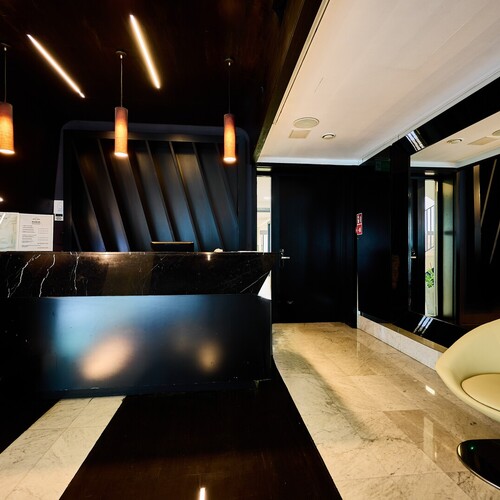 검은 대리석 카운터, 따뜻한 펜던트 조명, 거울 벽과 노란 라운지 의자가 있는 현대적 호텔 리셉션