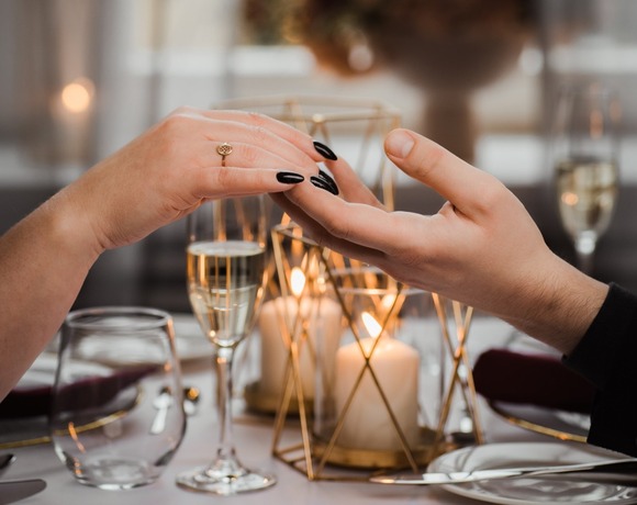 Mains d’un couple se tenant au‑dessus d’une table aux bougies, flûtes de champagne et centre floral