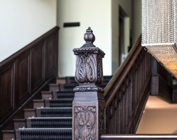 Escalier en bois sculpté avec pilier décoratif, tapis à motif et lustre de cristal en cascade dans un intérieur d'hôtel élégant