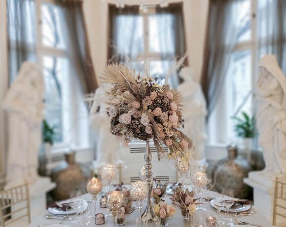 Elegant round dining table for formal dinner, crystal chandelier overhead, tall floral centerpiece, candles and place settings.