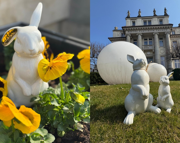 네오클래식 호텔 앞 잔디에 놓인 흰 도자기 토끼 조각들과 큰 흰 구체, 한 토끼가 노란 팬지 사이에 있음.