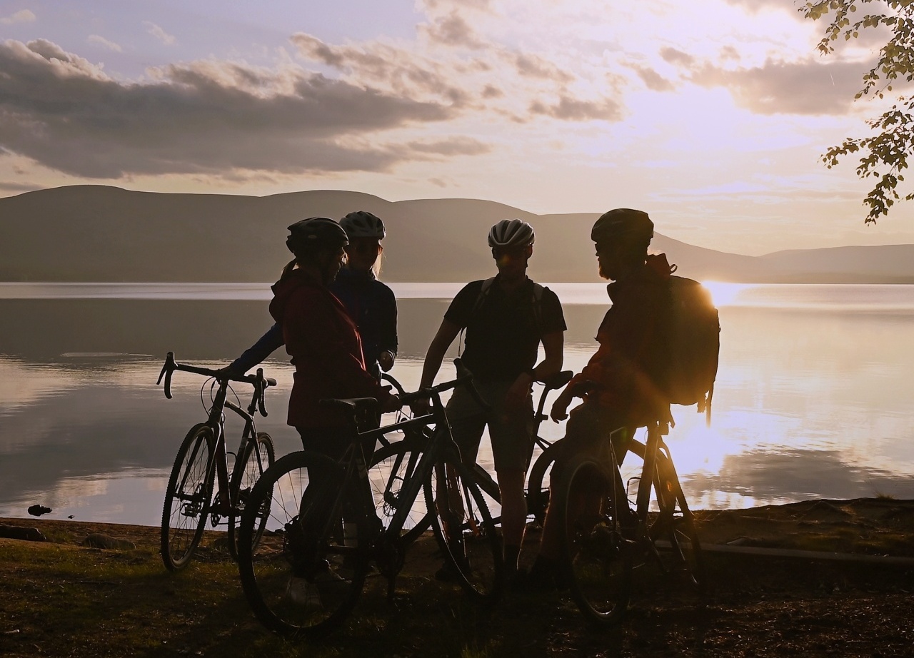 Cyclists silhouetted at a tranquil lakeshore at sunset, mountain views and leafy shore — ideal for hotel bike tours and lakeside excursions.