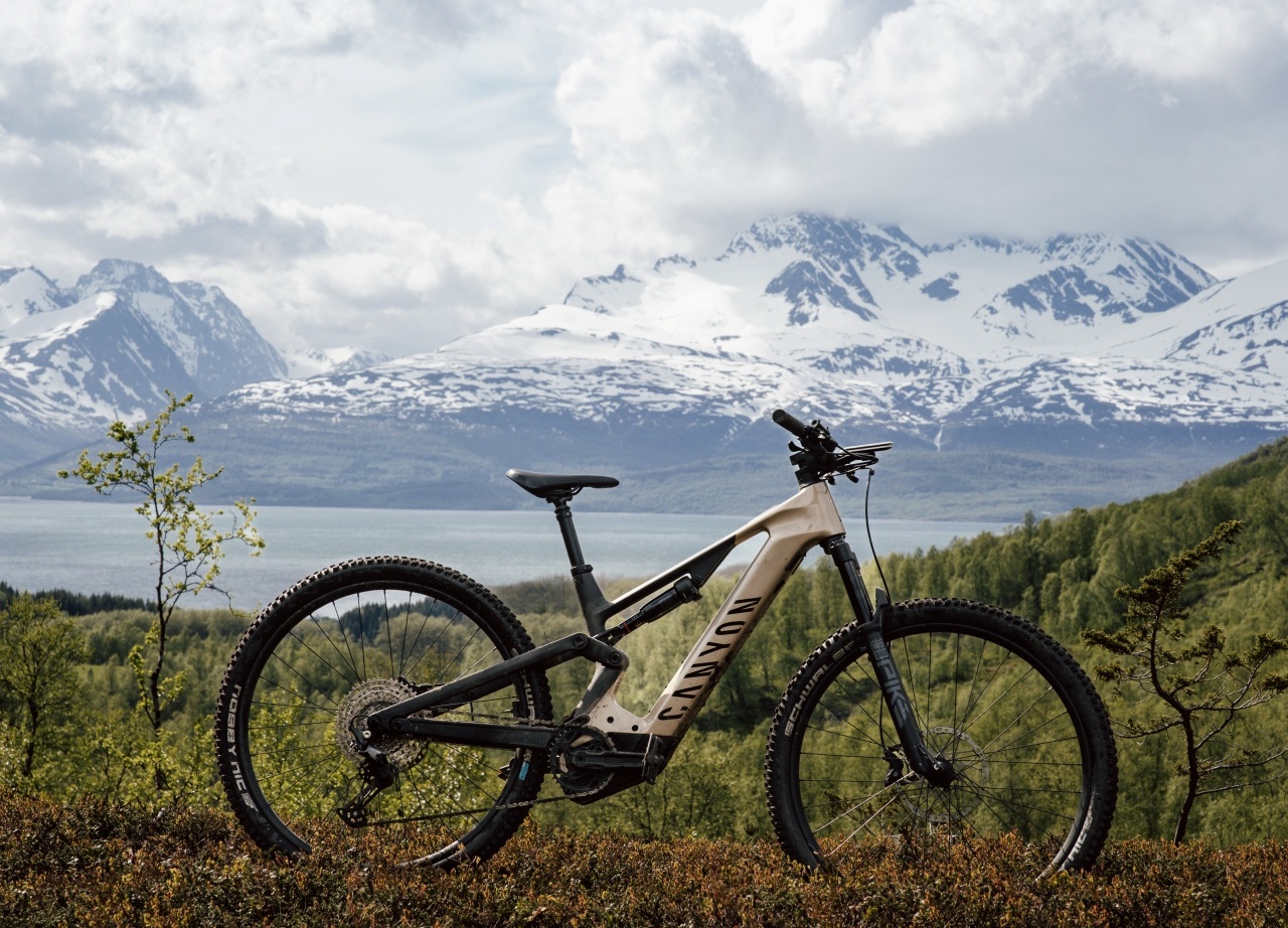 Mountain bike parked on a heath overlooking a lake and snow‑capped mountains beneath a dramatic cloudy sky