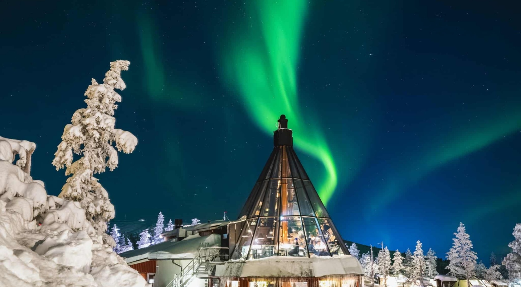 Glass-walled rooftop lounge and observation deck with warm interior, beneath vivid green Northern Lights and snow-covered pine trees