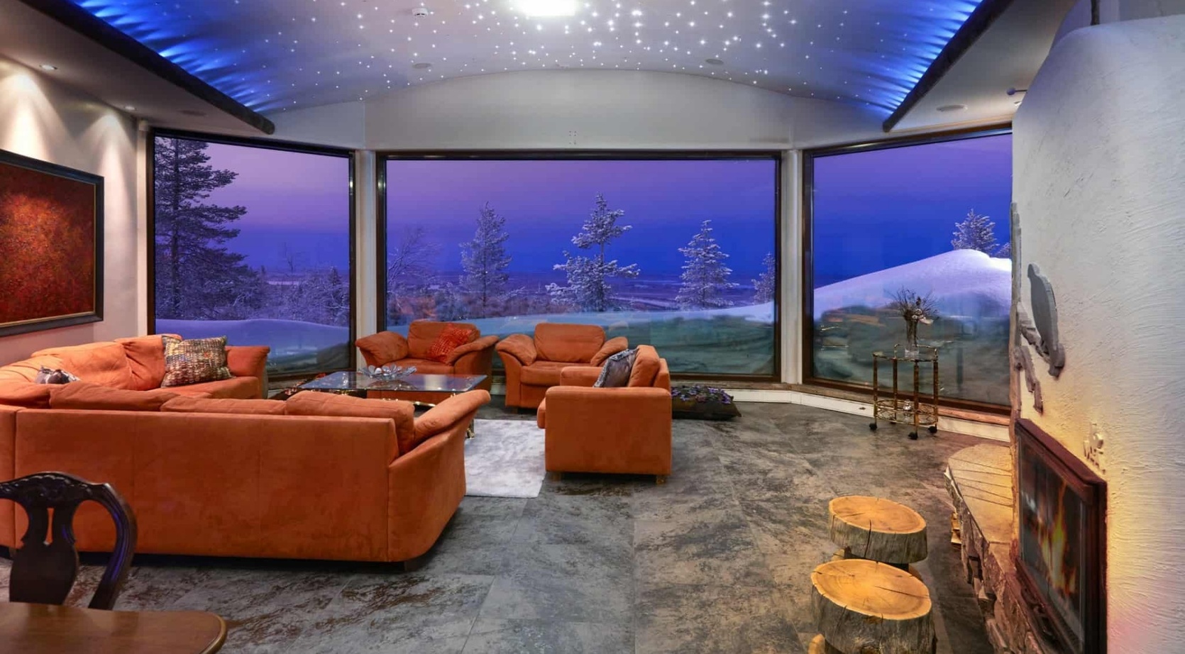 Cozy lodge lounge with panoramic floor-to-ceiling windows framing snowy forest at dusk, orange sofas, starry LED ceiling, fireplace and rustic wood-stump stools