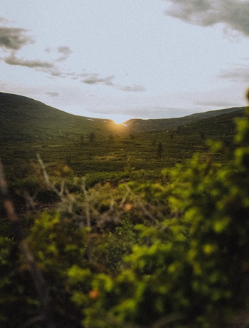 Sunset light between two hills over green moorland, lush foreground, calm setting for hiking and nature retreats
