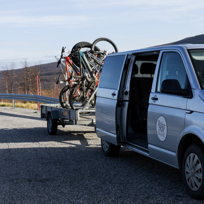 Tour shuttle van with Polar Star Travel logo and bike trailer parked on a scenic mountain road, ready for guided cycling excursions.