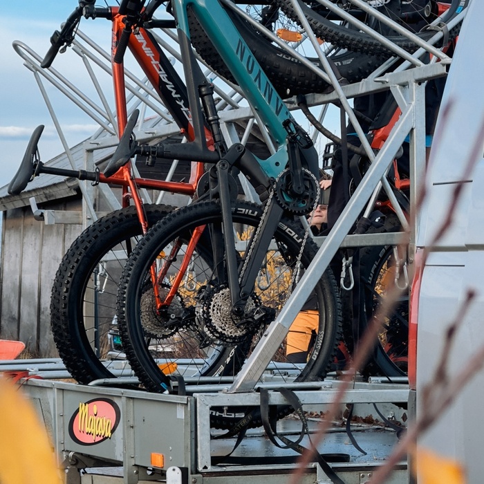 Three mountain bikes with fat tires locked vertically on a metal trailer rack, teal and red frames; person adjusting bikes.