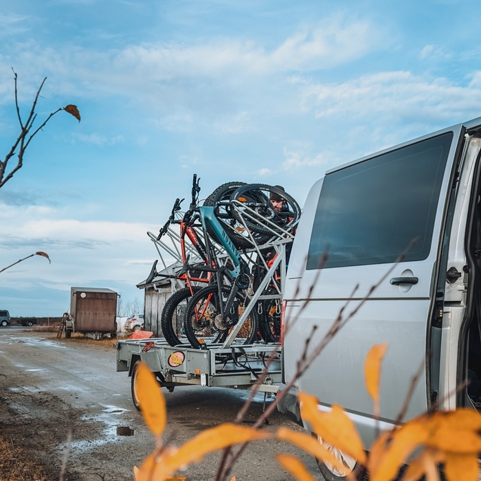 Shuttle van with multiple mountain bikes mounted on a trailer amid autumn foliage, ready for guided hotel bike tours.