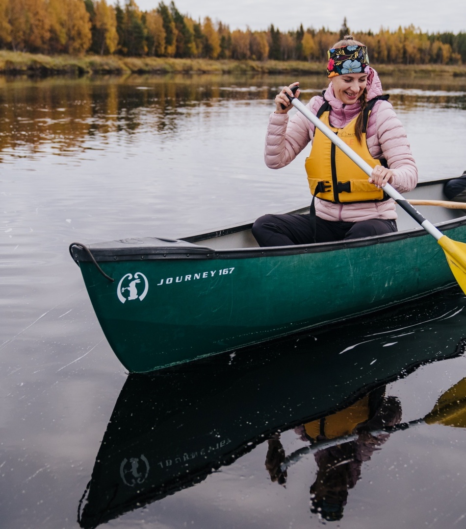 Couple paddling a green canoe on a calm autumn river, wearing life jackets and smiling