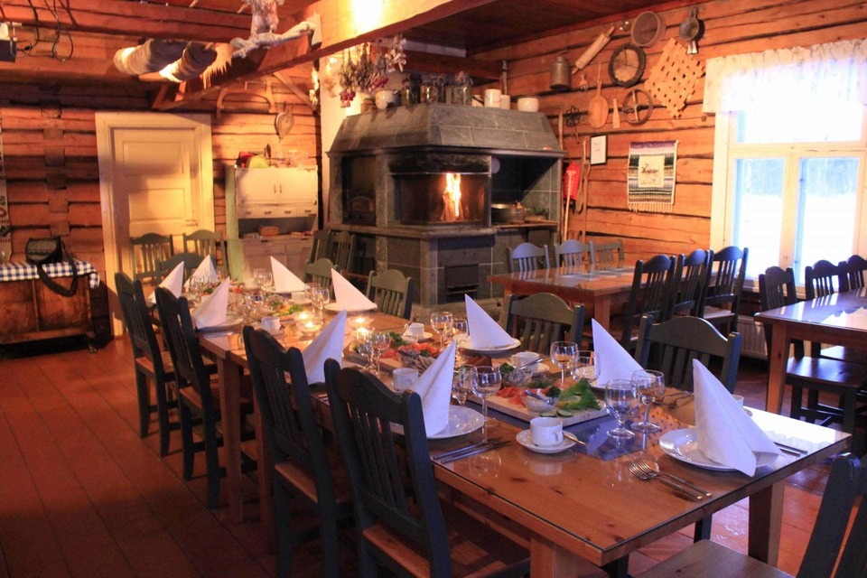 Rustic log cabin dining room with long wooden tables set for a communal meal, napkins, cozy stone fireplace and warm light