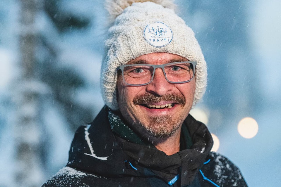 Smiling winter guide in snow-dusted jacket and Polar Star Travel knit hat, ready to lead outdoor snowy excursions.