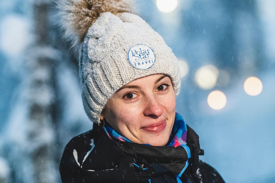 Smiling guest wearing a Polar Star Travel knit hat and warm jacket during a snowy evening excursion