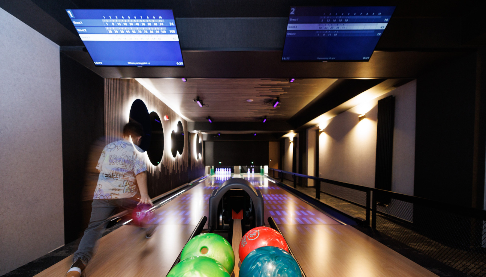 Hotel bowling lane with colorful balls, lit pins, modern ambient lighting and overhead score screens