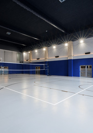Vnitřní víceúčelové hřiště s volejbalovou sítí, basketbalovými koši a házenkářskou brankou; světlá moderní tělocvična pro hosty.