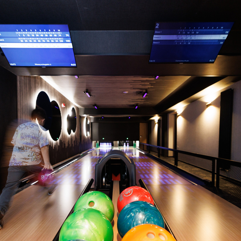 Bowlingová dráha v hotelu s barevnými koulemi v popředí, osvětlenými kuželkami, příjemným osvětlením a obrazovkami skóre