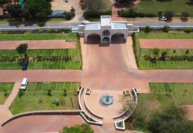 Aerial hotel entrance with white arched porte-cochère, circular fountain and curved benches, brick driveways and neat lawn parking.