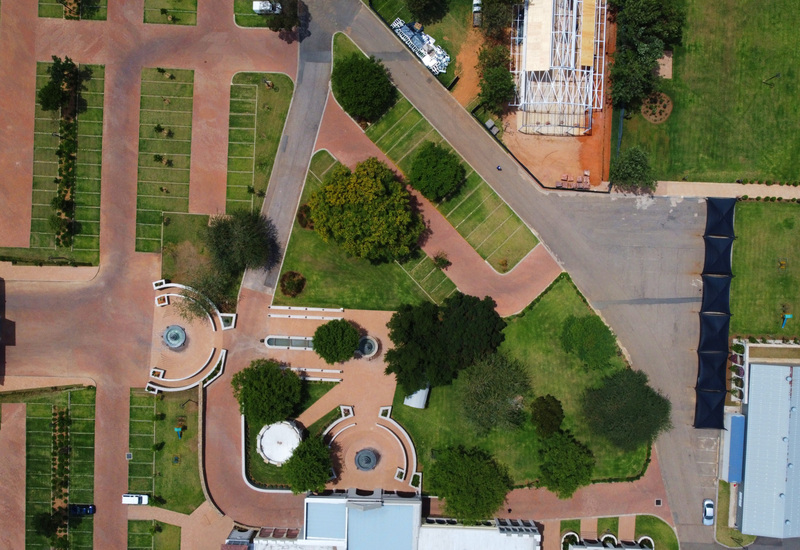 Aerial view of hotel entrance with twin circular fountains, tree-lined lawns, paved driveways and shaded parking canopies.
