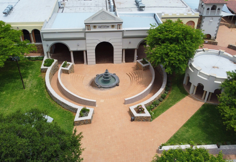 Convention center with colonnaded entrance, semicircular red-tile courtyard, tiered fountain, stone planters and shaded pavilion