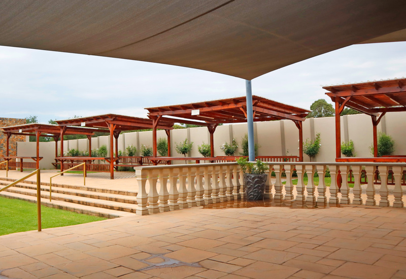 Shaded outdoor terrace with tiled patio, stone balustrade, steps to lawn and wooden pergolas with seating for events