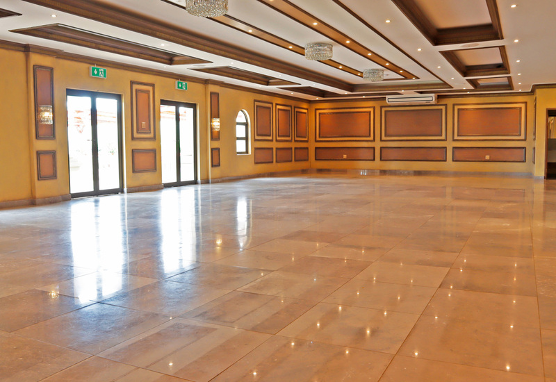 Hotel ballroom with polished marble floor, crystal chandeliers, coffered ceiling, paneled walls and glass doors to terrace.