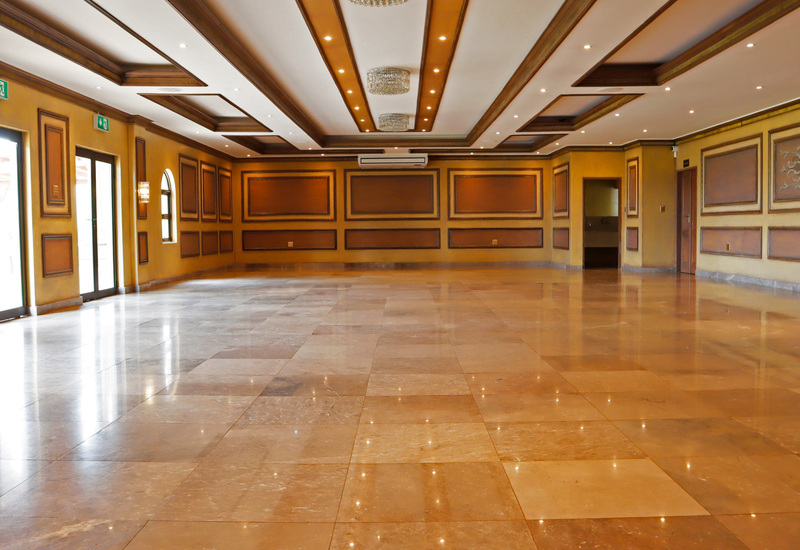Grand empty banquet hall with polished marble floor, coffered ceiling, crystal chandeliers, warm paneled walls and glass doors to terrace.