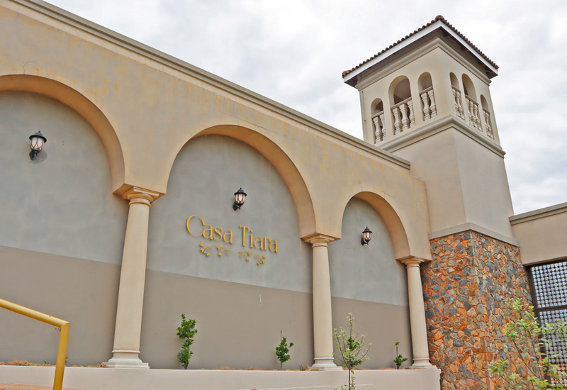 Mediterranean-style hotel entrance 'Casa Tiara' with arched colonnade, stucco facade, stone tower and exterior lanterns.