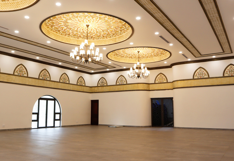 Grand banquet hall with ornate golden ceiling medallions, chandeliers, arched windows and wide open event floor.